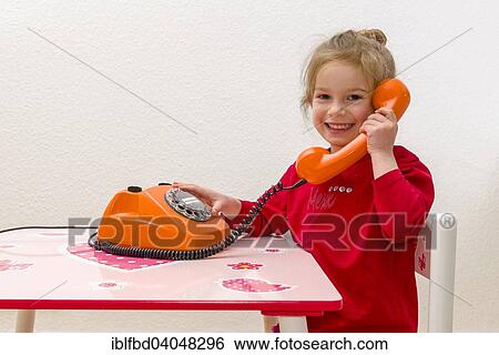 "Girl, 3 years, sitting at a table and using an orange telephone" View Large Photo Image Stock Photograph - "Girl, 3 years, sitting at a table and using an orange telephone". Fotosearch