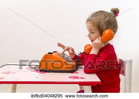 Stock Photography - "Girl, 3 years, sitting at a table and using an orange telephone". Fotosearch