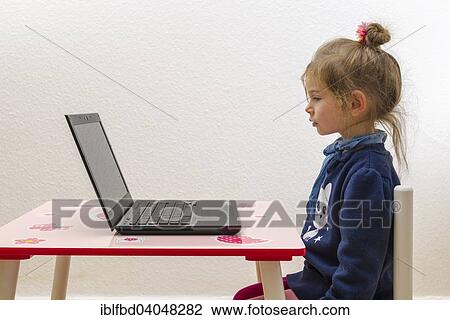 Stock Image - "Girl, 3 years, sitting at a table, in front of a laptop". Fotosearch