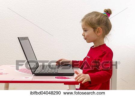 Stock Image - "Girl, 3 years, sitting at a table, using a laptop". Fotosearch