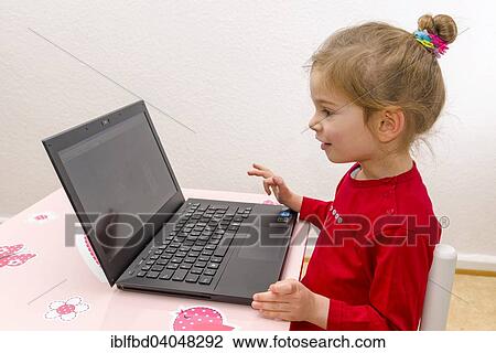 Stock Image - "Girl, 3 years, sitting at a table, using a laptop". Fotosearch