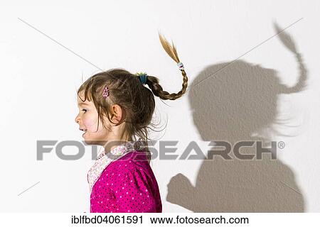 Stock Image - "Girl, 3 years, wearing a pink shirt, dancing, casting a shadow on a white wall". Fotosearch