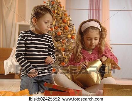 Stock Image - Girl and boy unpacking gifts in front of a Christmas tree. Fotosearch