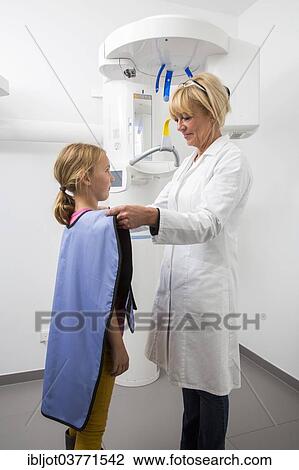 Stock Image - "Girl being prepared for an x-ray of her teeth, wearing a lead vest as radiation protection, Germany, Europe". Fotosearch