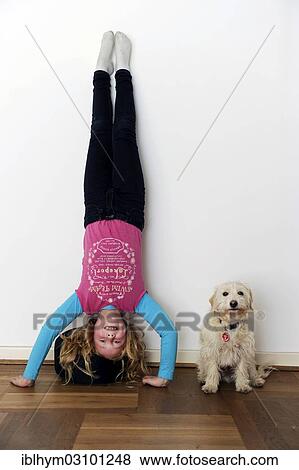 Stock Photo - "Girl doing a headstand, dog sitting next to her, Germany, Europe". Fotosearch