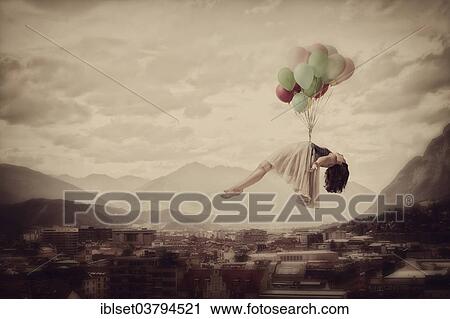 Stock Image - Girl hovering with balloons in the sky over a city. Fotosearch