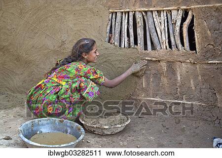 Stock Image - "Girl in traditional dress plastering the wall of a house with a mixture of water, sand and cow dung, Rann of Kutch, Gujarat, India, Asia". Fotosearch