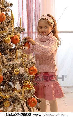 Stock Photo - Girl lighting a candle of a festively decorated Christmas tree. Fotosearch