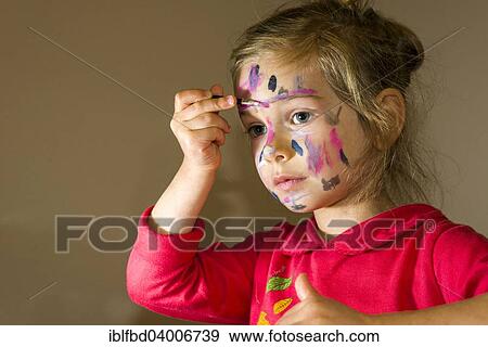 Stock Photo - "Girl painting her face with colourful watercolour, Germany, Europe". Fotosearch