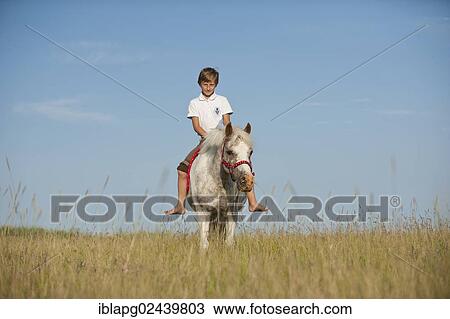 Stock Image - Girl riding a pony across a meadow. Fotosearch
