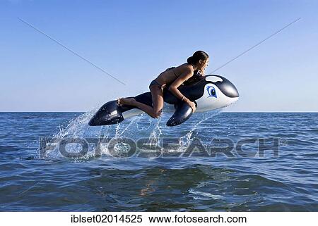 Stock Photography - Girl sitting on inflatable orca jumping in the sea. Fotosearch