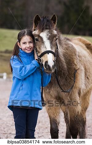 Picture - "Girl standing beside a pony, dun, with a bridle, Tyrol, Austria, Europe". Fotosearch