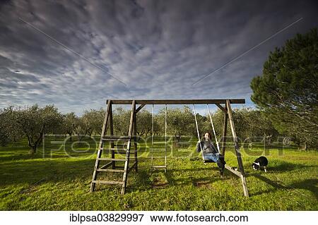 Stock Photo - "Girl swinging on a wooden swing in front of an olive grove, Tuscany, Italy, Europe". Fotosearch