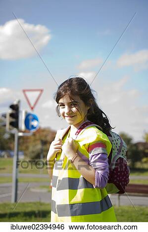 Stock Photograph - Girl with a school bag wearing a safety vest in front of a road sign. Fotosearch