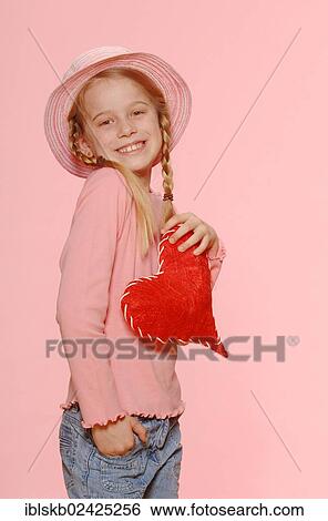 Stock Photograph - "Girl with braids, wearing a hat and holding a red heart". Fotosearch