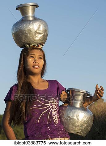 Stock Photography - "Girl with tanaka in her face carries water vessels made of aluminum, Laymyethna Pagoda or Temple, Mrauk U, Sittwe Division, Rakhine State, Myanmar, Asia". Fotosearch