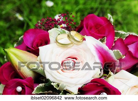 Stock Image - Golden wedding rings on a bridal bouquet with pink roses. Fotosearch