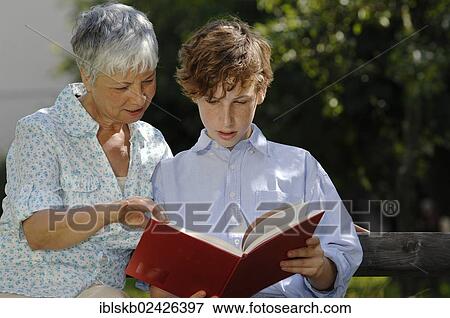 Stock Photo - Grandmother and grandson are looking at a red book together on park bench. Fotosearch