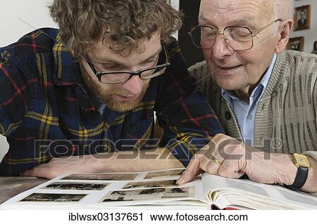 Stock Image - "Grandson and grandfather looking at photos in a photo album, Emmendingen, Baden-Wurttemberg, Germany, Europe". Fotosearch