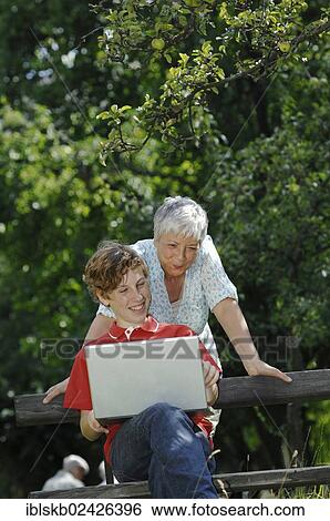 Grandson and grandmother looking together at a laptop computer on a park bench View Large Photo Image Stock Photograph - Grandson and grandmother looking together at a laptop computer on a park bench. Fotosearch