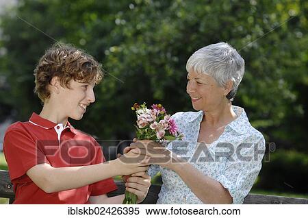Stock Photography - "Grandson gives his grandmother a bunch of flowers, on a park bench". Fotosearch