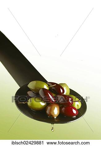 Stock Image - Green and black olives on a spoon with drops of oil. Fotosearch
