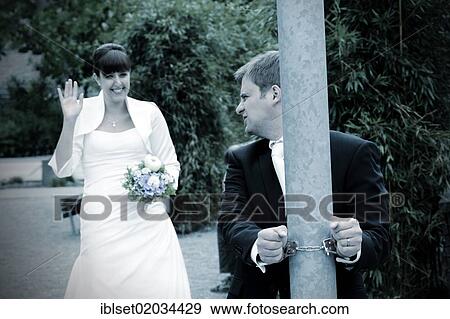Stock Photo - Groom is handcuffed to a pole while the bride waves and smiles. Fotosearch