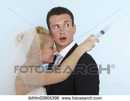 "Groom looking puzzled over his shoulder at a syringe in the hand of his smiling bride, Germany, Europe" View Large Photo Image Stock Photograph - "Groom looking puzzled over his shoulder at a syringe in the hand of his smiling bride, Germany, Europe". Fotosearch