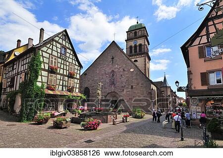 Stock Photograph - "Half-timbered house and fountain in front of the Church of Sainte-Croix on the Rue du General de Gaulle, Kaysersberg, Alsace, Haut-Rhin, France, Europe". Fotosearch
