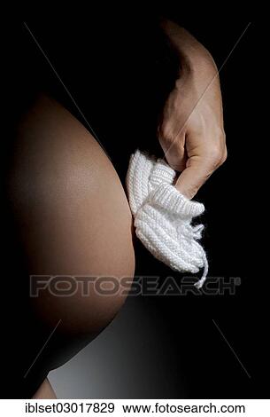 Stock Photo - Hand making white baby shoes walk on a pregnant belly. Fotosearch