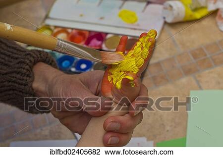 Stock Image - Hand of a little child getting painted with acrylic paint to create a handprint. Fotosearch