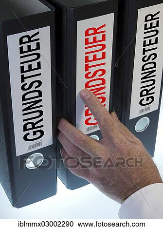 Stock Image - "Hand reaching for file folders labeled """"Grundsteuer"""", German for """"land tax""""". Fotosearch
