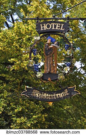 Stock Photo - "Hanging shop sign of the Hotel Meistertrunk, behind a blooming summer linden (Tilia platyphyllos), Rothenburg ob der Tauber, Middle Franconia, Bavaria, Germany, Europe". Fotosearch
