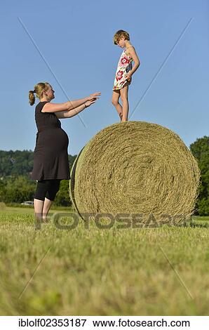 Stock Photo - "Heavily pregnant women, nine months, and girl, six years, standing on a straw bale, Germany, Europe". Fotosearch