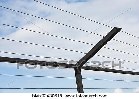Stock Photo - High fence with steel bars and wire against blue sky and clouds. Fotosearch