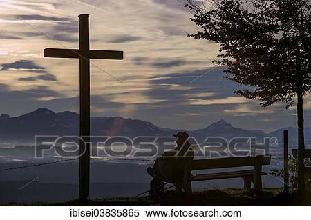 "Hiker sitting on a bench next to a cross, with a panoramic view of the Alps, Auerberg, Ostallgau, Bavaria, Germany, Europe" View Large Photo Image Stock Photography - "Hiker sitting on a bench next to a cross, with a panoramic view of the Alps, Auerberg, Ostallgau, Bavaria, Germany, Europe". Fotosearch