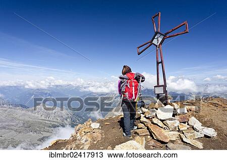 Stock Image - Hiker standing next to the summit cross on Schneebiger Nock mountain, province of Bolzano-Bozen, Italy, Europe. Fotosearch