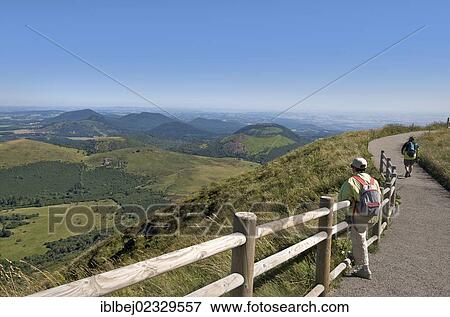 Stock Photo - "Hiker with view from Puy de Dome onto the volcanic landscape of the Chaine des Puys, Auvergne, France, Europe". Fotosearch