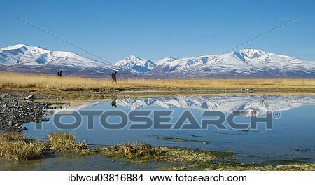 Picture - "Hikers at Khurgan Nuur, mirrored in the lake in front of mountains of the Altai Mountains, the region bordering China, Altai-Tawan Bogd National Park, Tsengel, Bajan-Olgii, High Altai Mountains, Mongolia, Asia". Fotosearch