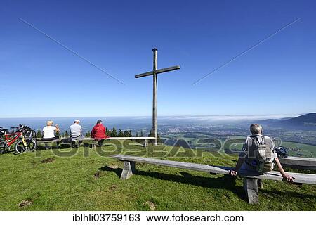 Stock Image - "Hikers at the summit cross on Blomberg Mountain, view over the Isar Valley with Bad Toelz and Wackersberg Mountain, Isarwinkel, Bad Tolz, Upper Bavaria, Bavaria, Germany, Europe". Fotosearch