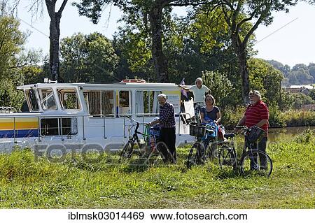 Stock Photo - "Holidaymakers in front of a house boat on the Canal des Vosges, formerly Canal de l'Est, after going shopping by bicycle, Girancourt, Epinal, Lorraine, Departement Vosges, France, Europe". Fotosearch