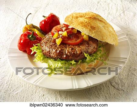 Stock Image - "Home made burger in a crusty roll with tomato sweetcorn relish, onion and BBQ peppers". Fotosearch