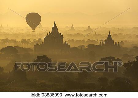 Stock Image - "Hot air balloon over the landscape in the early morning fog, temples, stupas, pagodas, temple complex, Plateau of Bagan, Mandalay Division, Burma or Myanmar". Fotosearch