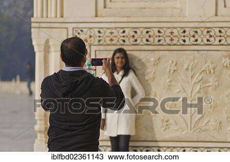 Stock Image - "Indian tourist taking a photograph of his wife at Taj Mahal, Agra, India, Asia". Fotosearch