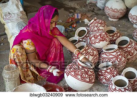 Stock Photo - "Indian woman wearing a headscarf sitting on the floor and painted clay water jars with traditional ornamentations, Jodhpur, Rajasthan, India, Asia". Fotosearch
