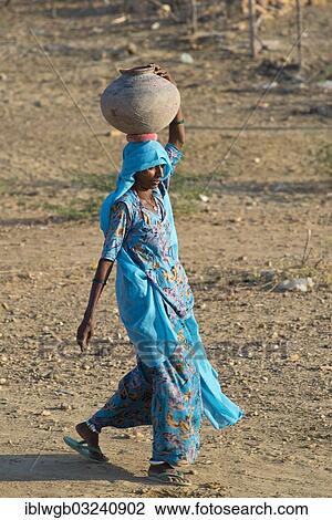 Stock Image - "Indian woman wearing a light blue sari carrying a clay water jug? Çï? Çïon her head, Khuri, Rajasthan, India, Asia". Fotosearch