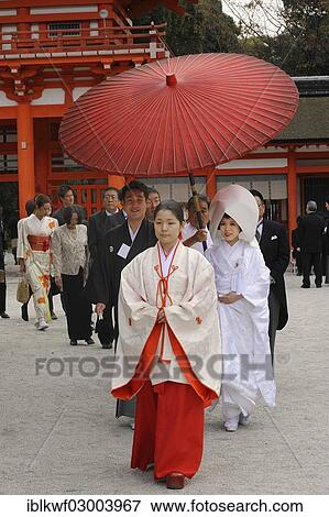 Stock Photo - "Japanese woman wearing scarlet hakama pants and a white kimono shirt with lengthy sleeves, in front of the gatehouse of Shimogamo Shrine, Kyoto, Kinki region, Japan, Asia". Fotosearch