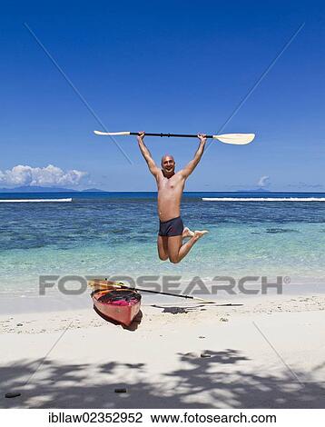 Stock Image - "Kayaker jumping for joy on a beach, Seychelles, Africa, Indian Ocean, Africa". Fotosearch