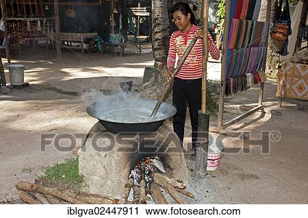Stock Image - "Khmer woman stirring palm sap in a traditional heated metal boiler to produce palm sugar, Siem Reap, Cambodia, Southeast Asia, Asia". Fotosearch