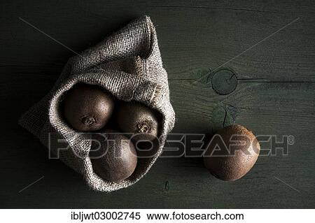 Stock Photography - Kiwi fruits in jute sack lying on a wooden table. Fotosearch